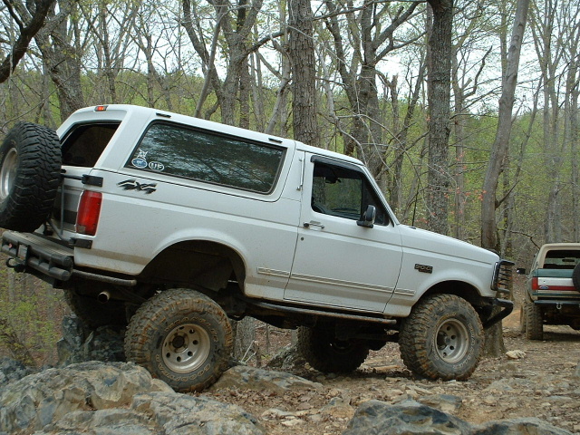 White Ford Bronco with spare tire on rear, navigating rocky terrain