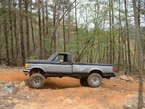 1987 Ford F-150 - A lifted 1987 Ford F-150 navigates a rocky, wooded trail.