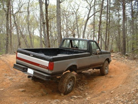 1987 Ford F-150 - This two-tone Ford pickup truck navigates a wooded trail, its off-road capabilities.