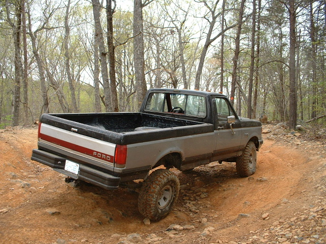 1987 Ford F-150 pickup truck, rear 3/4 view, on dirt trail
