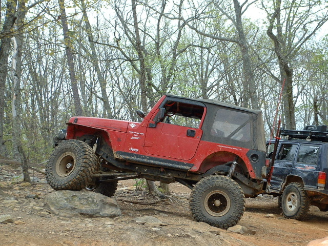Red Jeep Wrangler on rocks, another Jeep behind it. Off-road tires visible