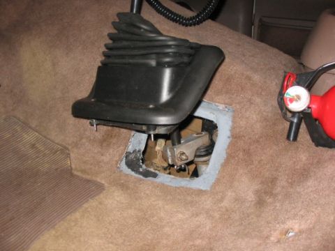 1995 Ford Bronco - The interior of a vehicle shows the manual transmission shifter and the exposed transfer case linkage, along with a fire extinguisher.