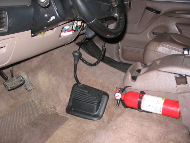 Vehicle interior floor with black shifter boot, tan carpet, and red fire extinguisher