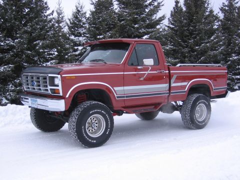 1984 Ford F-150 - Lifted red Ford pickup truck with custom decals parked in a snowy landscape.