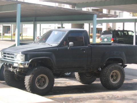 1991 Ford Bronco - A modified pickup truck with a lifted suspension and oversized tires sits parked under a covered area.