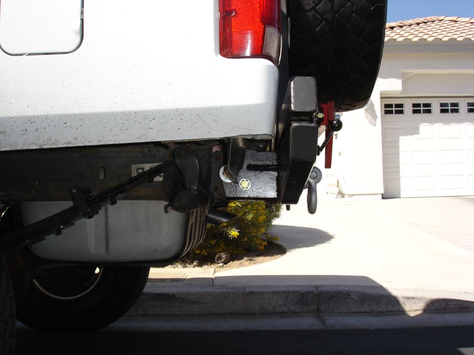 Black custom rear bumper with hitch and D-ring on a white SUV in a driveway