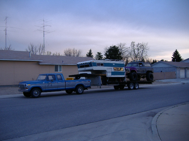 Blue Ford pickup truck towing a trailer with a camper and a lifted purple SUV on it