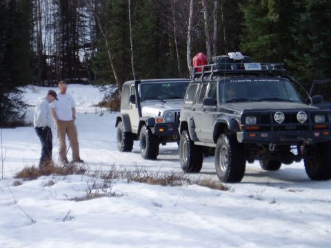 2000 Ford E350 - Several off-road vehicles are parked in a snowy, wooded area. Two people stand next to the lead Jeep.