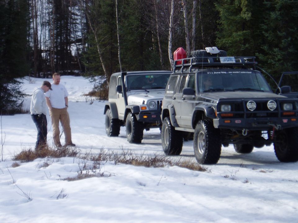 Two Jeeps and a Jeep Cherokee parked in snow with two people standing nearby