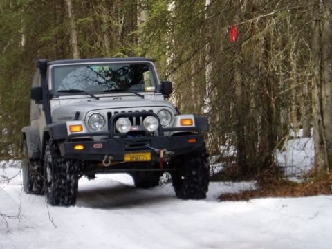 2000 Ford E350 - Silver Jeep Wrangler Rubicon equipped for off-road driving in a snowy forest environment.