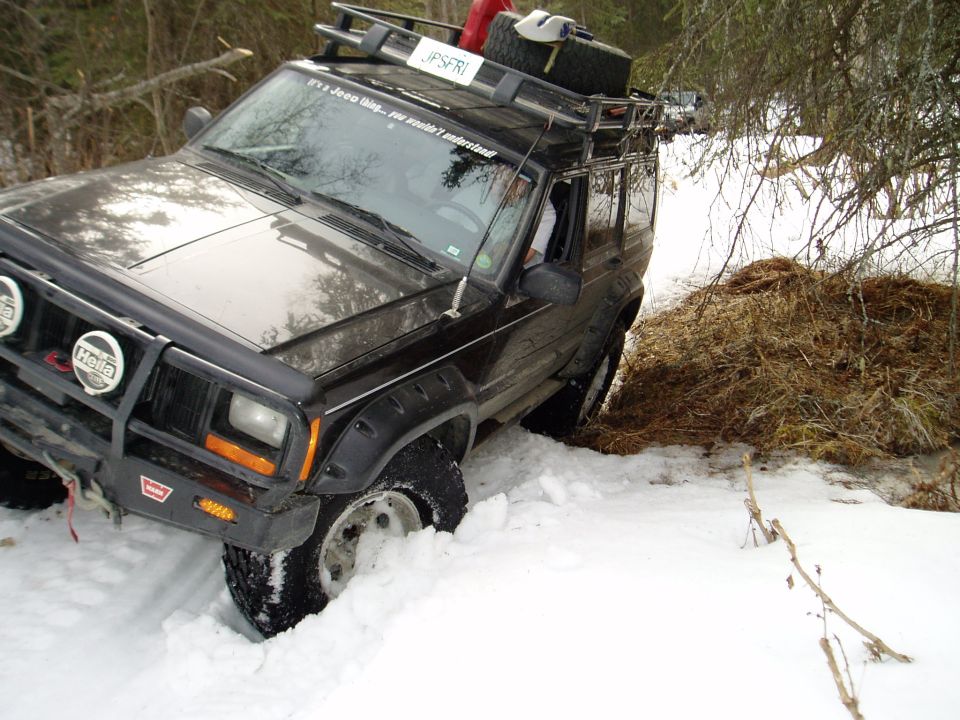 Black Jeep Cherokee with roof rack stuck in snow, front bull bar with Hella lights