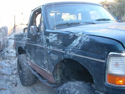 1984 Ford Bronco - Heavily damaged dark blue SUV on a rocky trail, likely a 1992-1996 Ford Bronco.