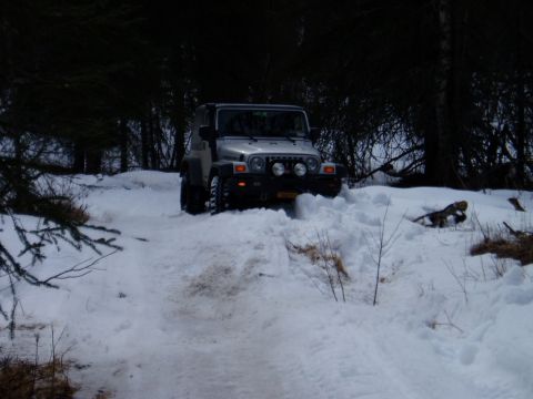 2000 Ford E350 - A silver Jeep Wrangler navigates a snow-covered trail, pushing through deep drifts.