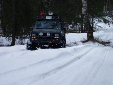 2000 Ford E350 - Modified Jeep Cherokee XJ navigates a snowy forest road with a roof rack and off-road lights.
