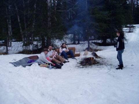 2000 Ford E350 - A group of people enjoy a campfire in a snowy, wooded area.