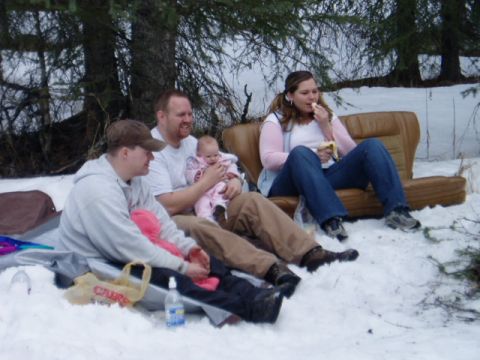 2000 Ford E350 - A group of people are gathered in the snow, some sitting on the ground and one on a couch, with a baby and snacks.