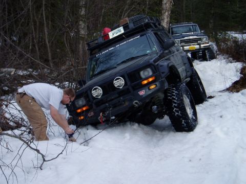 2000 Ford E350 - Off-road Jeep Cherokee XJ with modifications is stuck in the snow, while another Jeep waits behind it.