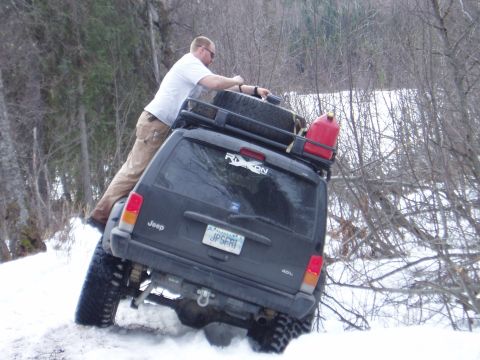 2000 Ford E350 - A Jeep Cherokee XJ is stuck in the snow with a man on its roof rack, a red gas can is also visible.