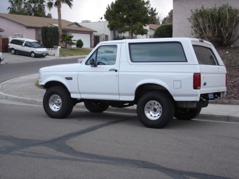 1996 Ford Bronco - A white Ford Bronco is parked on a suburban street, showing its lifted suspension and aftermarket wheels.