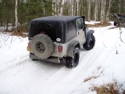 2000 Ford E350 - A Jeep Wrangler navigates a snow-covered path in a wooded area.