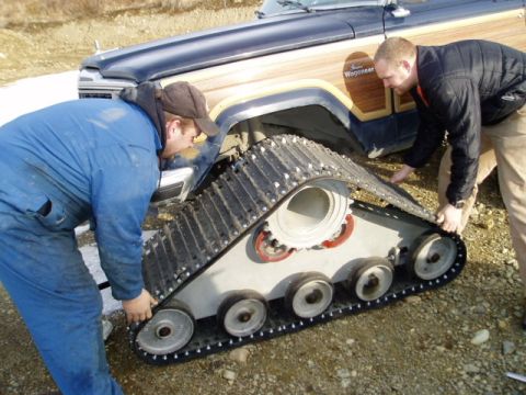 2000 Ford E350 - Two men examine a tank track next to a vintage wood-paneled SUV.