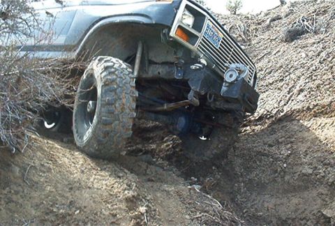 1986 Ford Bronco - A dark-colored Ford Bronco with large tires navigates a steep dirt incline.