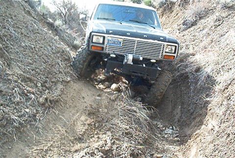 1986 Ford Bronco - This Ford Bronco is navigating a challenging off-road trail with steep, eroded sides.