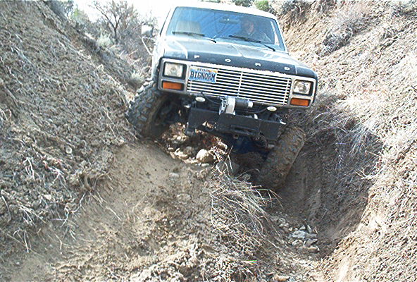 Ford Bronco driving down a steep, rocky ditch. License plate says BIGNORK