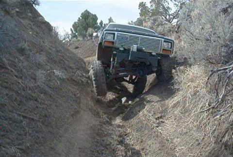 1986 Ford Bronco - A black Ford Bronco navigates a steep, narrow dirt trail in a dry, brushy environment.
