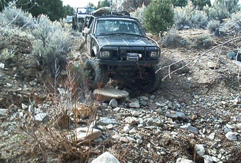 1986 Ford Bronco - Modified black SUV tackles a challenging off-road course with another vehicle visible behind it.