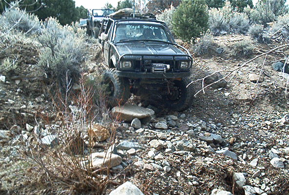 Black off-road SUV with winch and roof rack navigating rocky terrain