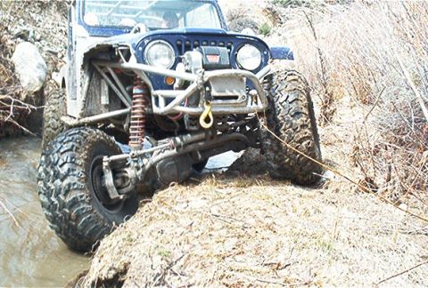 1986 Ford Bronco - This heavily modified off-road vehicle is shown navigating a challenging natural terrain with mud and vegetation.