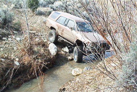 1986 Ford Bronco - This SUV is shown off-roading through a shallow stream with rocky terrain.