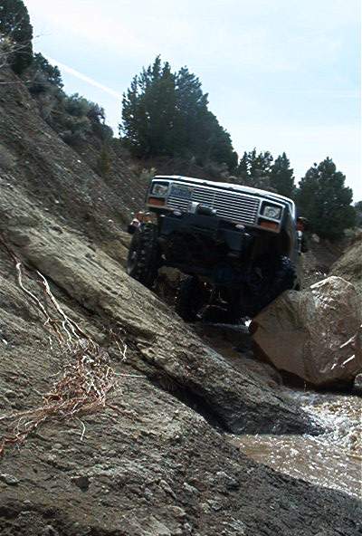1986 Ford Bronco - A black Jeep Cherokee navigates a challenging rocky terrain, its front grille clearly visible against the landscape.