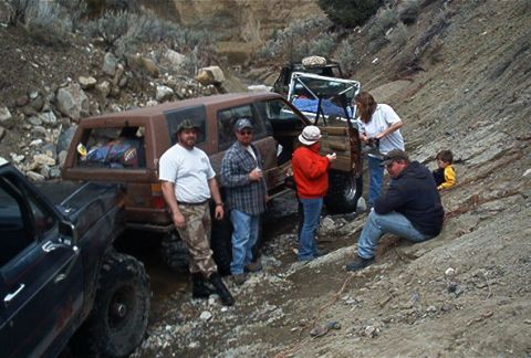 1986 Ford Bronco - A group of people and their off-road vehicles are stopped on a rocky, uneven terrain.