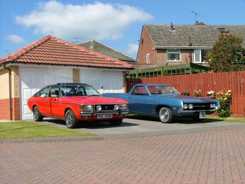1976 Ford Granada - A red coupe and a blue pickup truck are parked in a driveway on a sunny day.