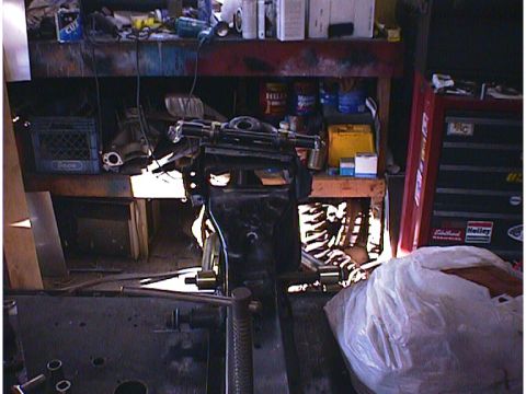 1960 Ford Falcon - An engine component is mounted on a stand in a workshop setting, surrounded by tools and supplies.