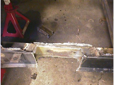 1960 Ford Falcon - Close-up of a car's frame undergoing repair work, with welding visible and a red jack stand in the background.