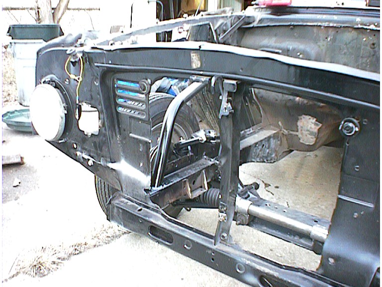 Stripped black car front end with exposed suspension and empty headlight bucket in a driveway