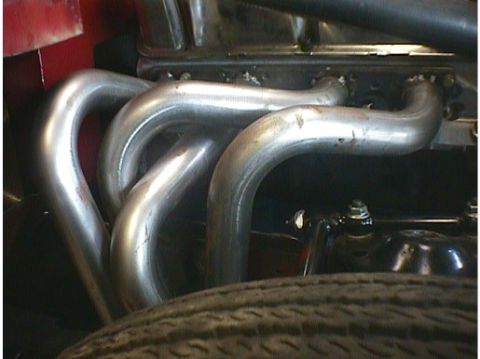 1960 Ford Falcon - Shiny exhaust headers are installed on the engine, with a tire peeking out from the bottom of the frame.