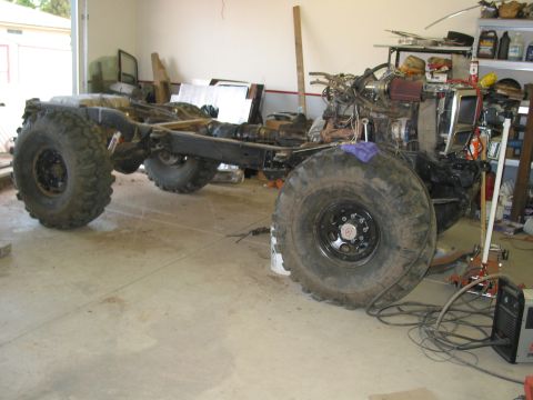 1981 Ford Bronco - This vehicle chassis, equipped with massive tires and an incomplete engine, is undergoing modifications in a workshop.