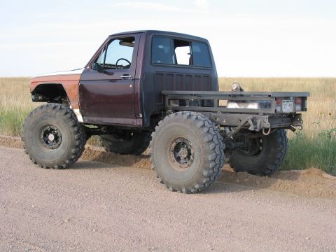 1981 Ford Bronco - This heavily modified truck sits on a dirt road with large off-road tires and a flatbed in the rear.