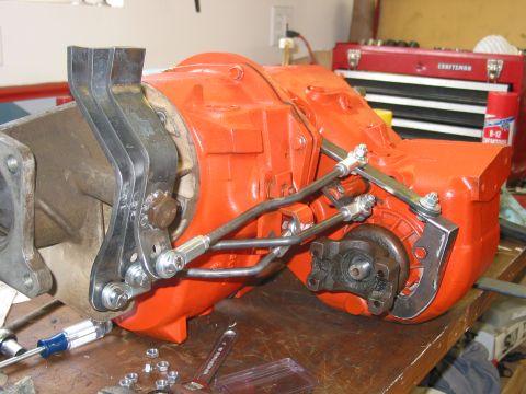 1981 Ford Bronco - Close-up of an orange transmission component with attached linkage, resting on a workbench.