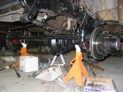 1981 Ford Bronco - Close-up view of the front axle and suspension system, supported by jack stands, with a Supermotors.net logo in the lower right corner.