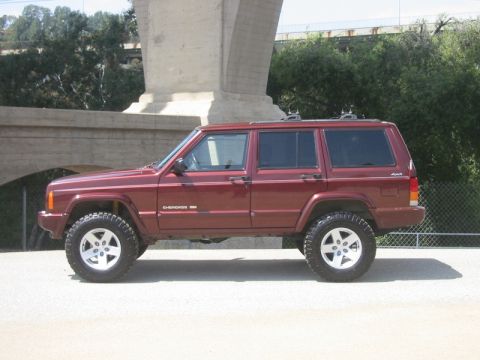 2000 Jeep Cherokee - A lifted 2000 Jeep Cherokee SUV is shown from the side, parked on pavement beneath a large concrete structure.