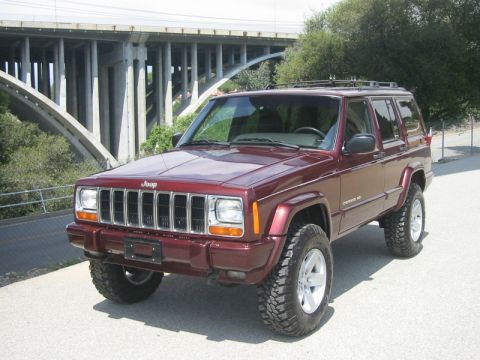 2000 Jeep Cherokee - This maroon Jeep Cherokee features a lifted suspension and aggressive off-road tires, parked outdoors with a bridge in the background.