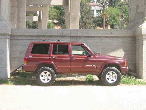 2000 Jeep Cherokee - A maroon Jeep Cherokee XJ is parked on a dirt patch next to a concrete wall, with a bridge overhead.