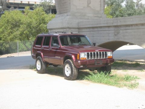 2000 Jeep Cherokee - This lifted Jeep Cherokee is parked on a dirt path beneath a large concrete structure.