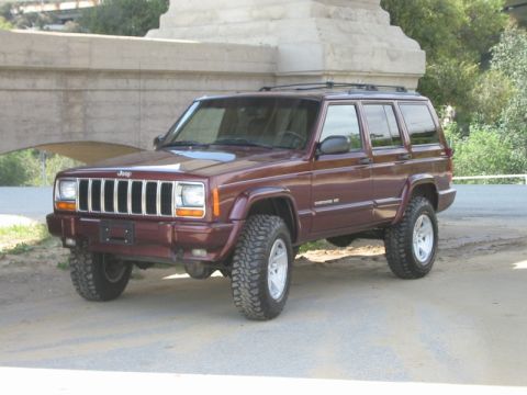 2000 Jeep Cherokee - This lifted Jeep Cherokee is shown from a three-quarter front angle, parked on a dirt surface.