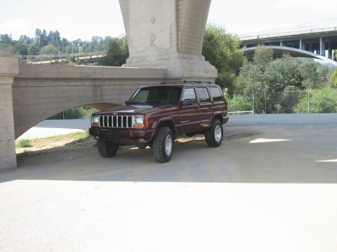 2000 Jeep Cherokee - This maroon 2000 Jeep Cherokee features a lifted suspension and is parked beneath a large concrete overpass.